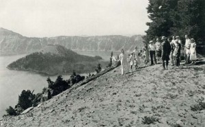 A Park Naturalist Tells the Story of Crater Lake, historic photograph Black and white print 8 1/2 x 5 1/4 inches Photographer: George Grant Description: To many visitors the morning hikes along the rim are highlights of the trip. Rangers who have studied the geology of the area explain rock formations and answer questions. Wizard Island, with its barren top above the trees, looks like a young volcano growing up in the caldera left when Mount Mazama disappeared.